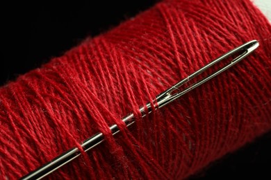 Photo of Spool of red sewing thread with needle on black background, closeup