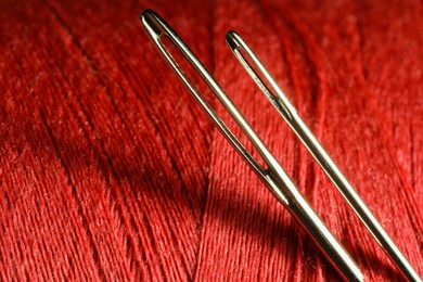 Photo of Spool of red sewing thread with needles, macro view