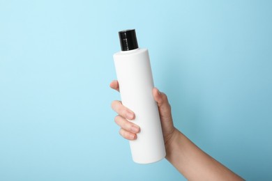 Photo of Woman with shampoo bottle on light blue background, closeup