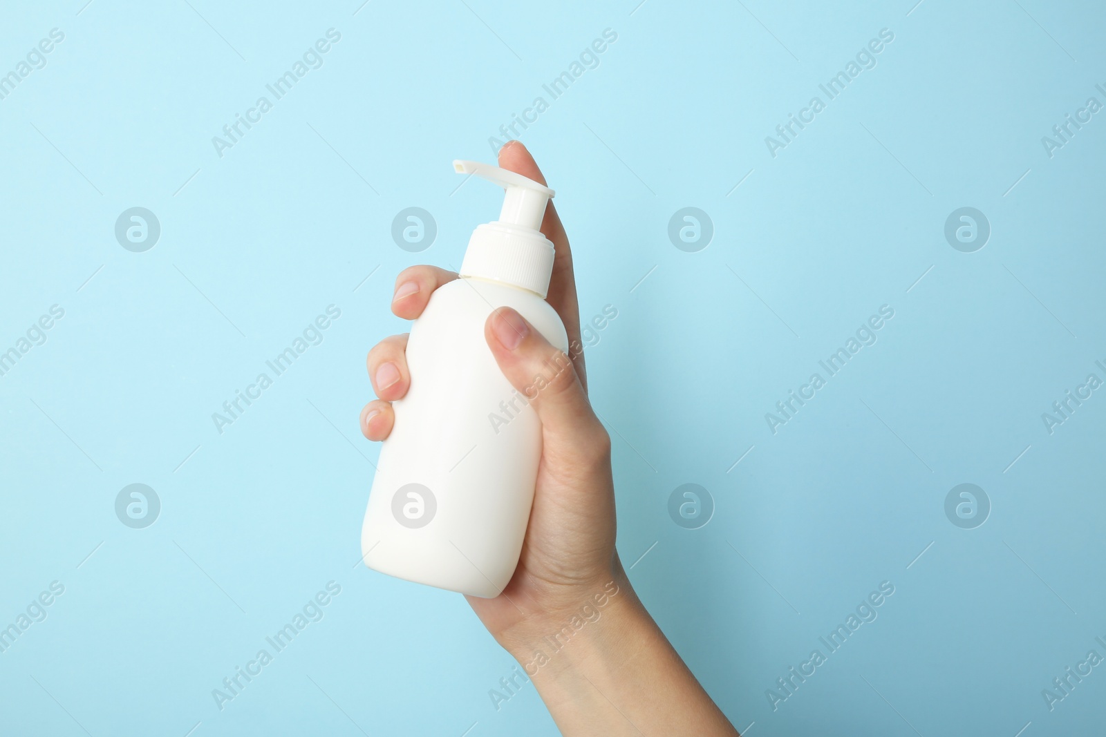 Photo of Woman with shampoo bottle on light blue background, closeup