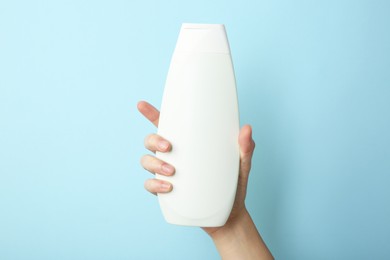 Photo of Woman with shampoo bottle on light blue background, closeup