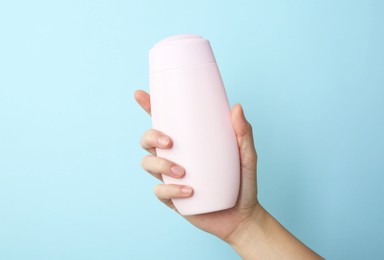 Photo of Woman with shampoo bottle on light blue background, closeup