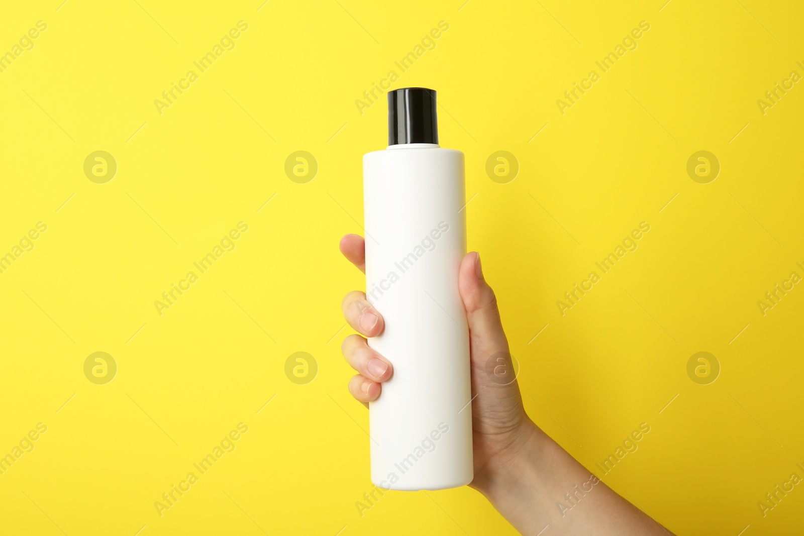 Photo of Woman with shampoo bottle on yellow background, closeup