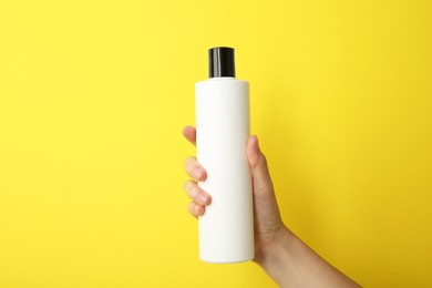 Photo of Woman with shampoo bottle on yellow background, closeup