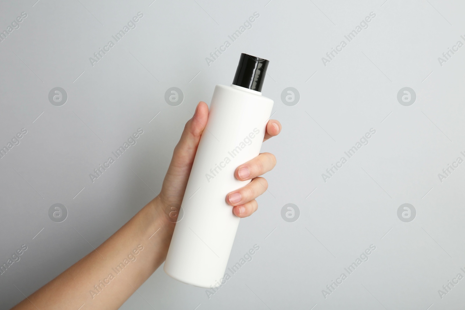 Photo of Woman with shampoo bottle on grey background, closeup