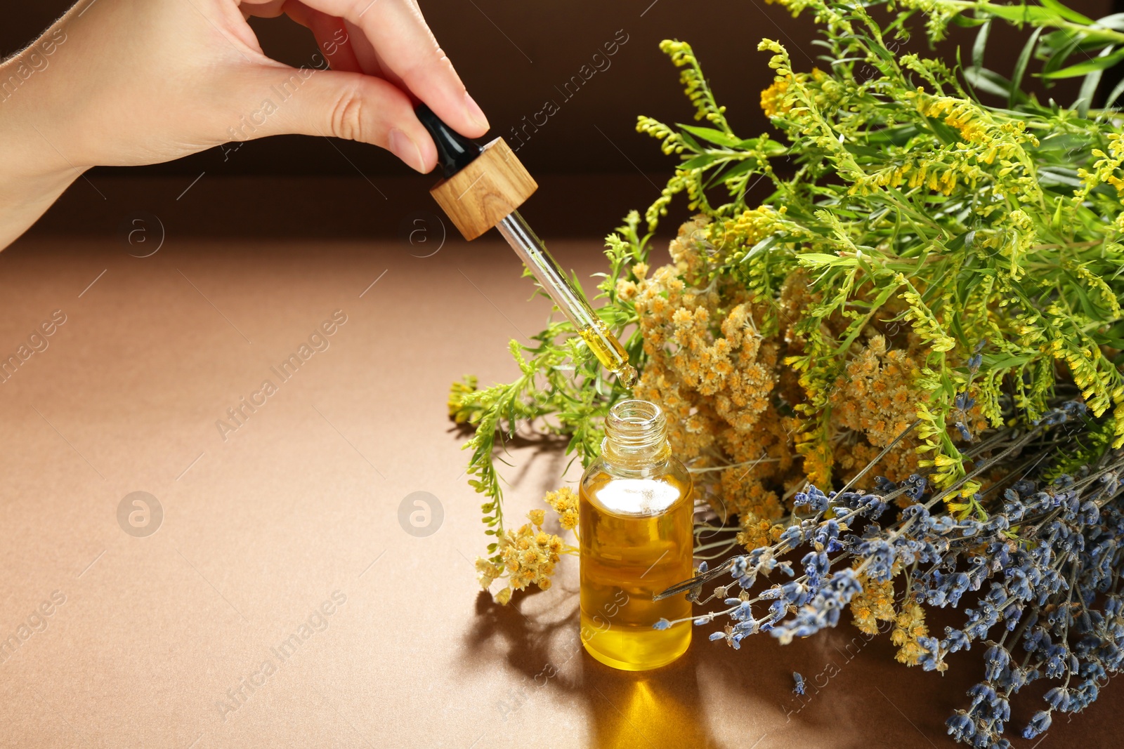 Photo of Woman dripping tincture from pipette into bottle and herbs on color background, closeup