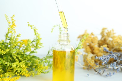 Dripping tincture from pipette into bottle and herbs on white background, closeup