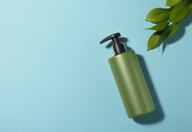 Photo of Bottle of shampoo and green leaves on light blue background, flat lay. Space for text