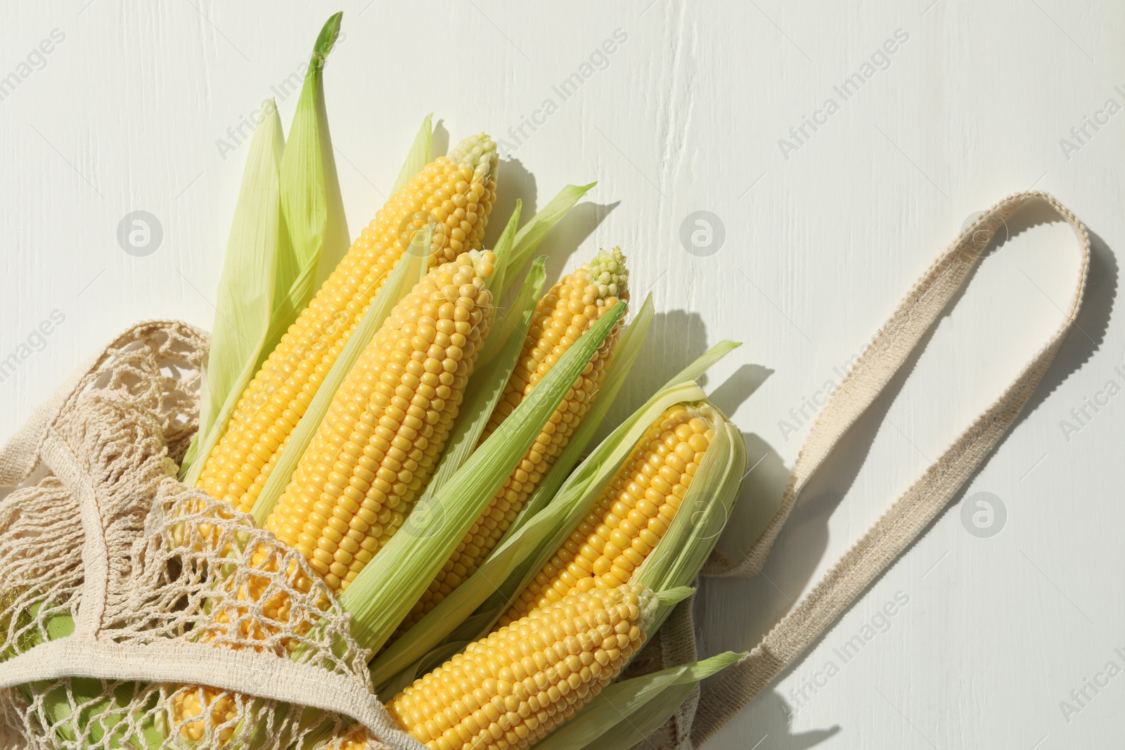 Photo of Many fresh ripe corncobs with green husks on white wooden table, top view