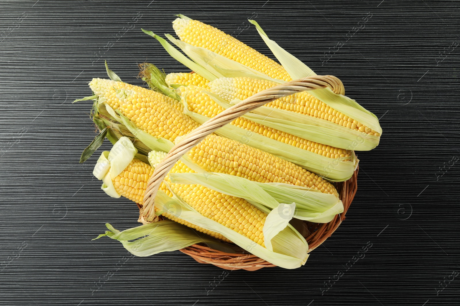 Photo of Many fresh ripe corncobs with green husks on wooden table, top view