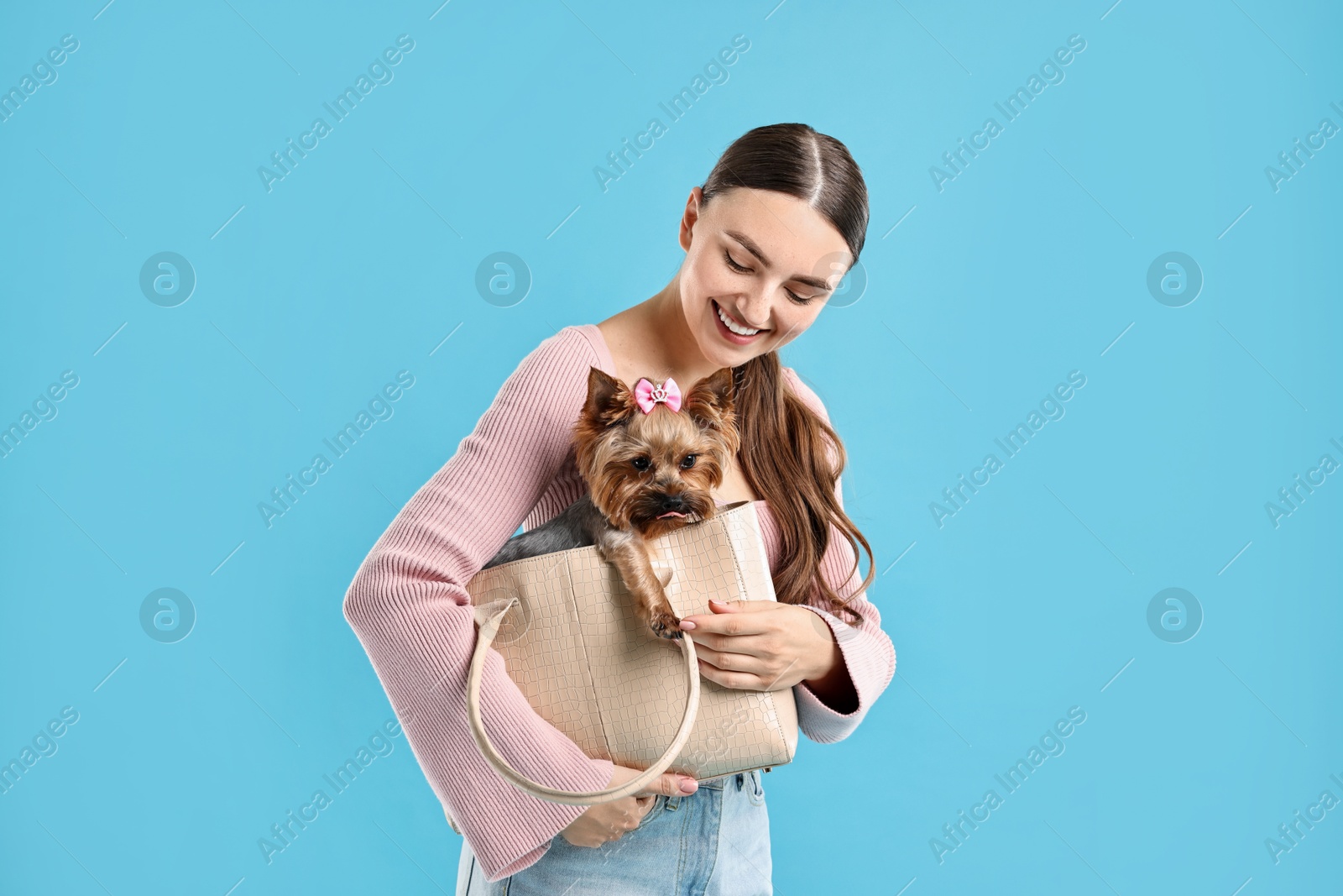 Photo of Beautiful young woman holding bag with cute Yorkshire Terrier dog on light blue background