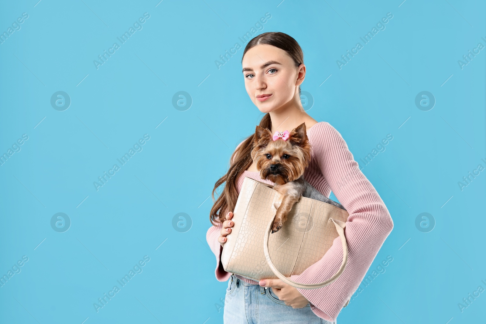 Photo of Beautiful young woman holding bag with cute Yorkshire Terrier dog on light blue background