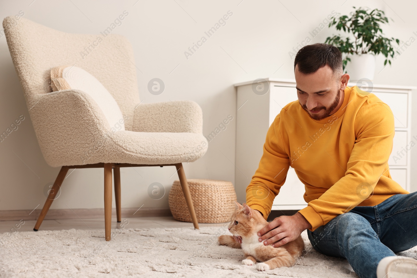 Photo of Man petting cute ginger cat on floor at home