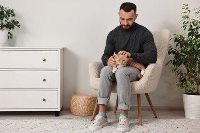 Man petting cute ginger cat on armchair at home