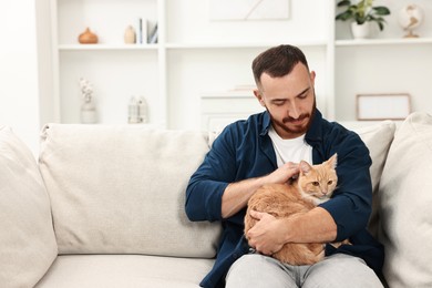 Man petting cute ginger cat on sofa at home, space for text