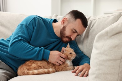 Man petting cute ginger cat on sofa at home