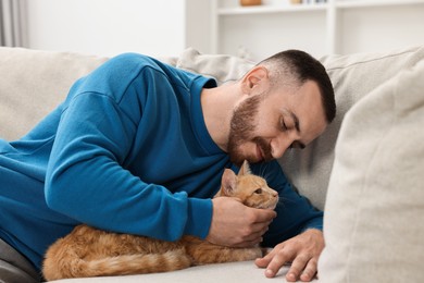 Man petting cute ginger cat on sofa at home