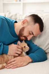 Man petting cute ginger cat on sofa at home