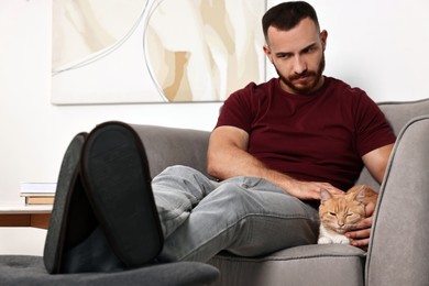 Man petting cute ginger cat on armchair at home