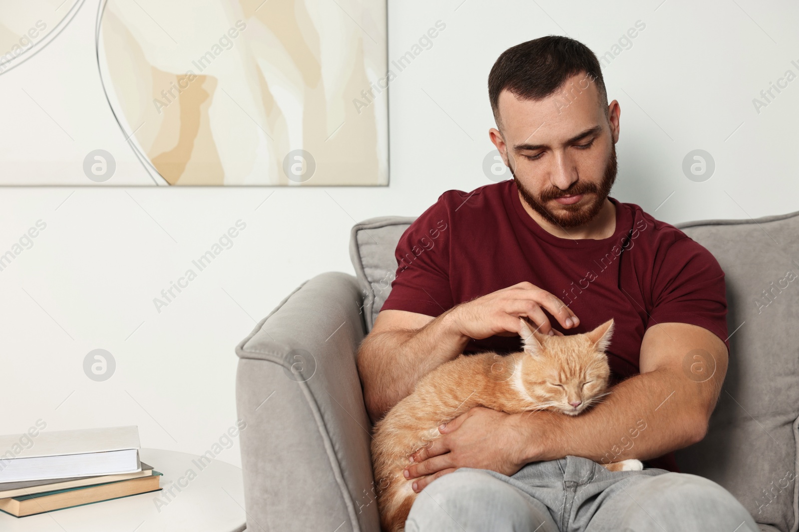 Photo of Man petting cute ginger cat on armchair at home, space for text