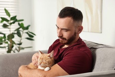 Man petting cute ginger cat on armchair at home