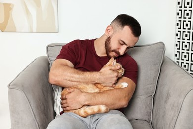 Photo of Man petting cute ginger cat on armchair at home