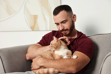 Photo of Man petting cute ginger cat on armchair at home