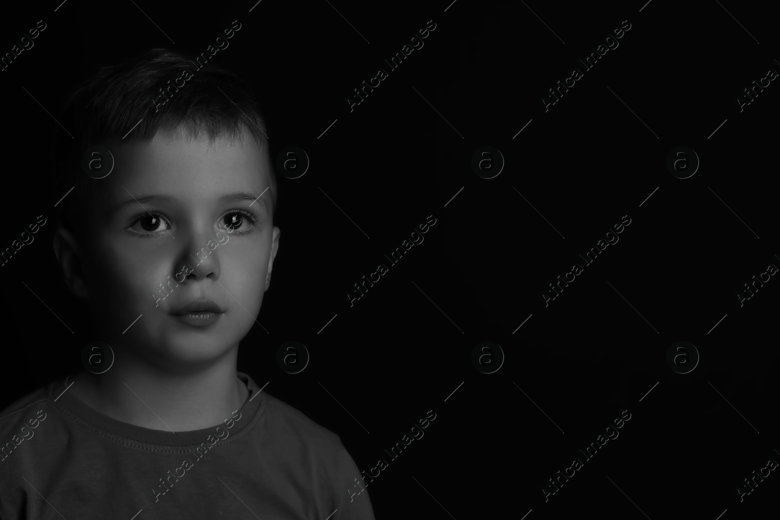 Photo of Portrait of sad little boy on dark background, space for text. Black and white effect