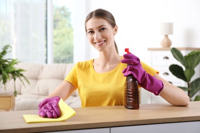 Young woman cleaning table with rag and spray at home