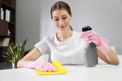 Photo of Young woman cleaning table with rag and spray in office