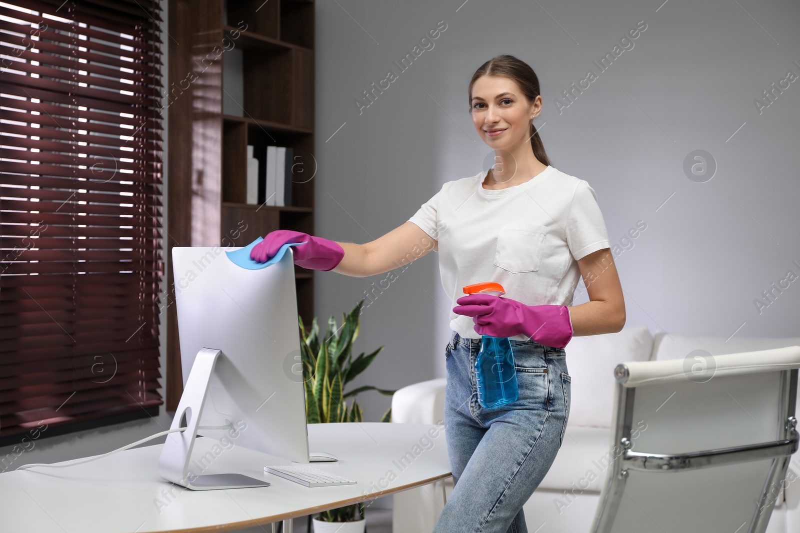 Photo of Young woman cleaning computer with rag and spray in office