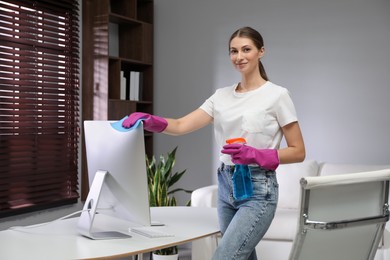 Young woman cleaning computer with rag and spray in office