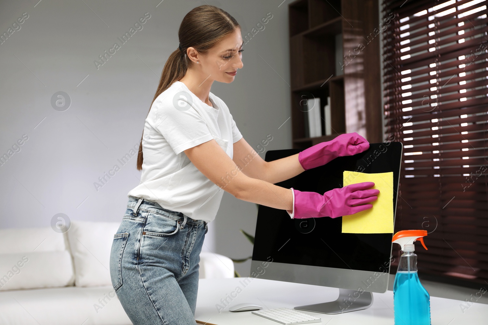 Photo of Young woman cleaning computer with rag and spray in office