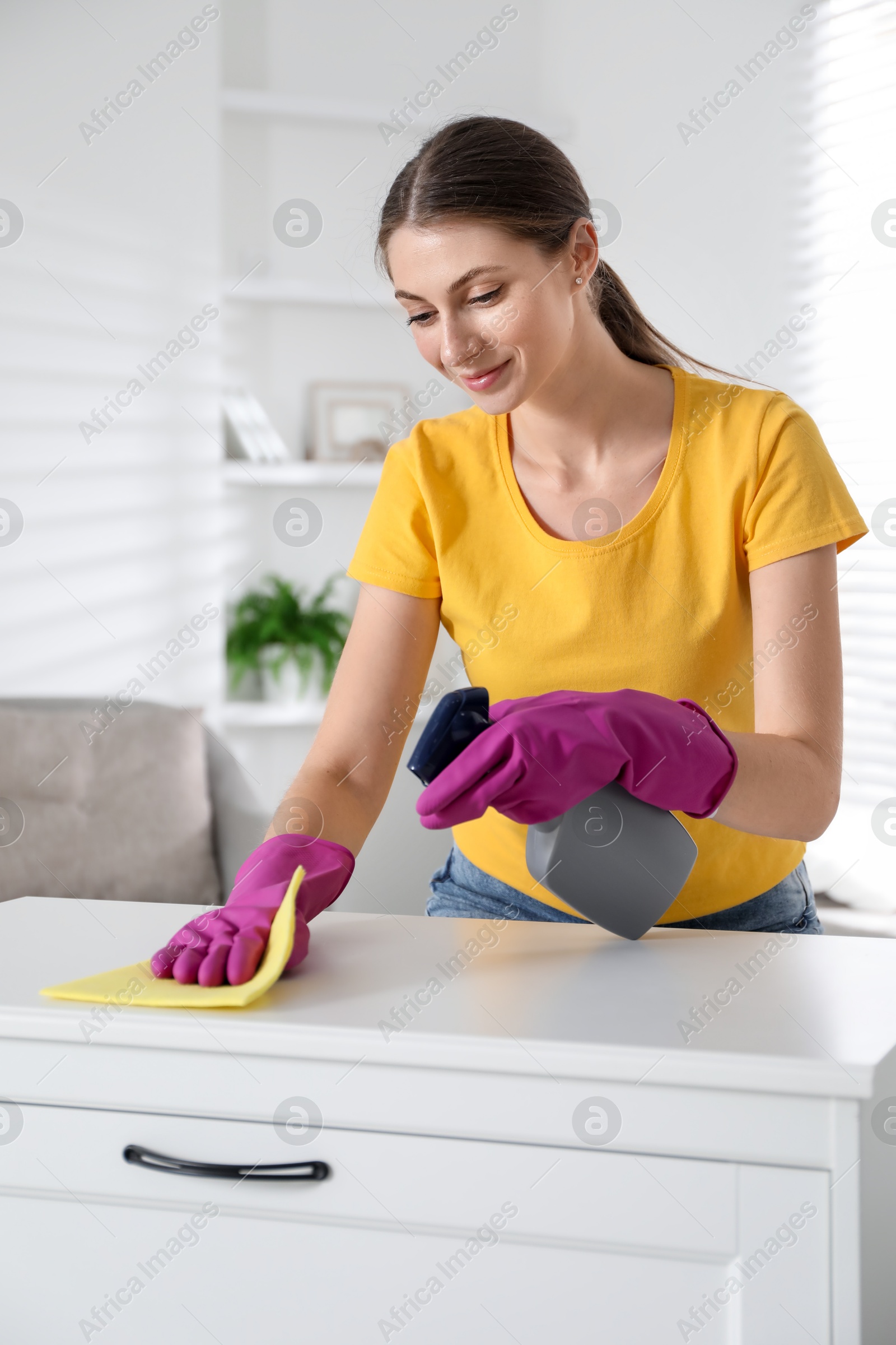 Photo of Young woman cleaning table with rag and spray in office