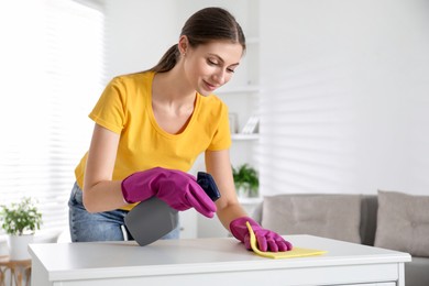 Young woman cleaning table with rag and spray in office