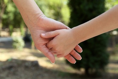 Photo of Mother and daughter holding hands in park, closeup