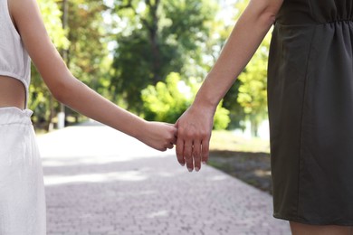 Photo of Mother and daughter holding hands in park, closeup