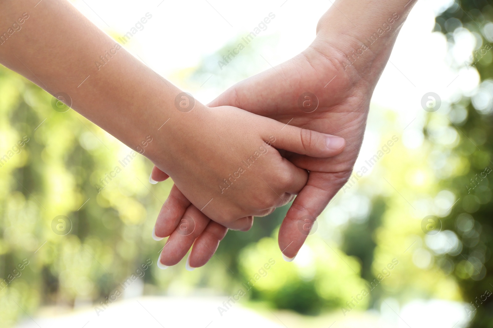 Photo of Mother and daughter holding hands in park, closeup