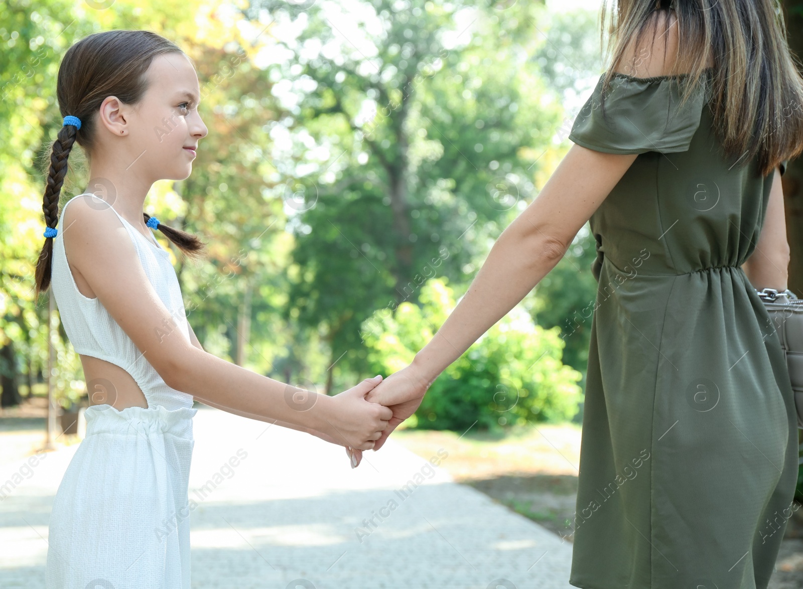 Photo of Little girl holding hands with mother in park, closeup