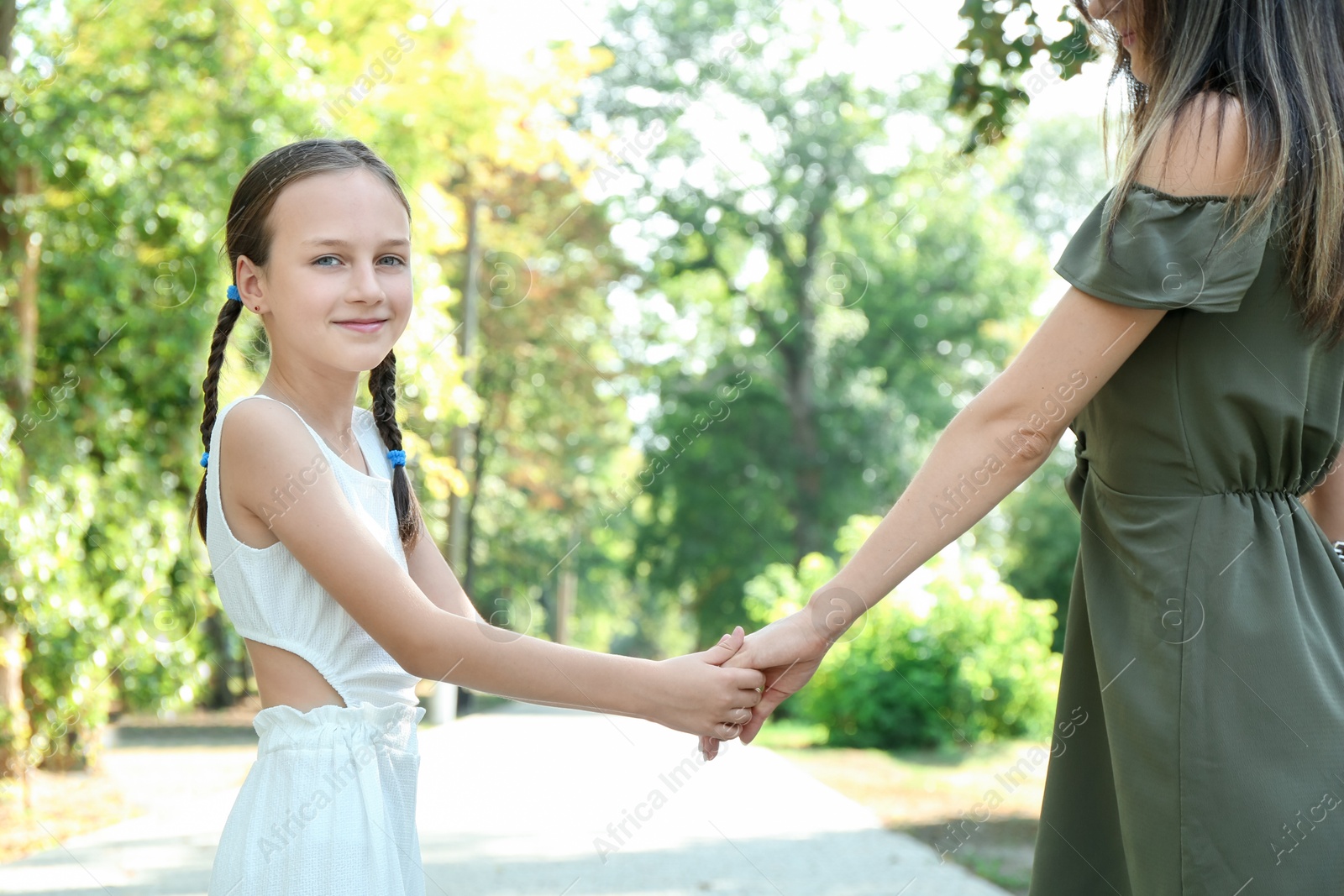 Photo of Little girl holding hands with mother in park, closeup