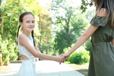 Photo of Little girl holding hands with mother in park, closeup