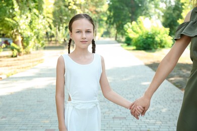 Photo of Little girl holding hands with mother in park, closeup