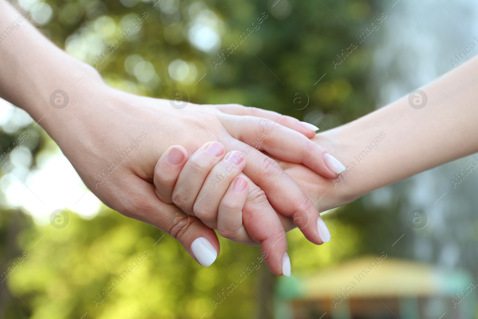 Photo of Mother and daughter holding hands in park, closeup