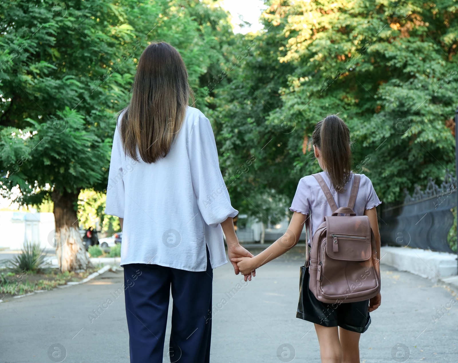 Photo of Mother and daughter holding hands outdoors, back view