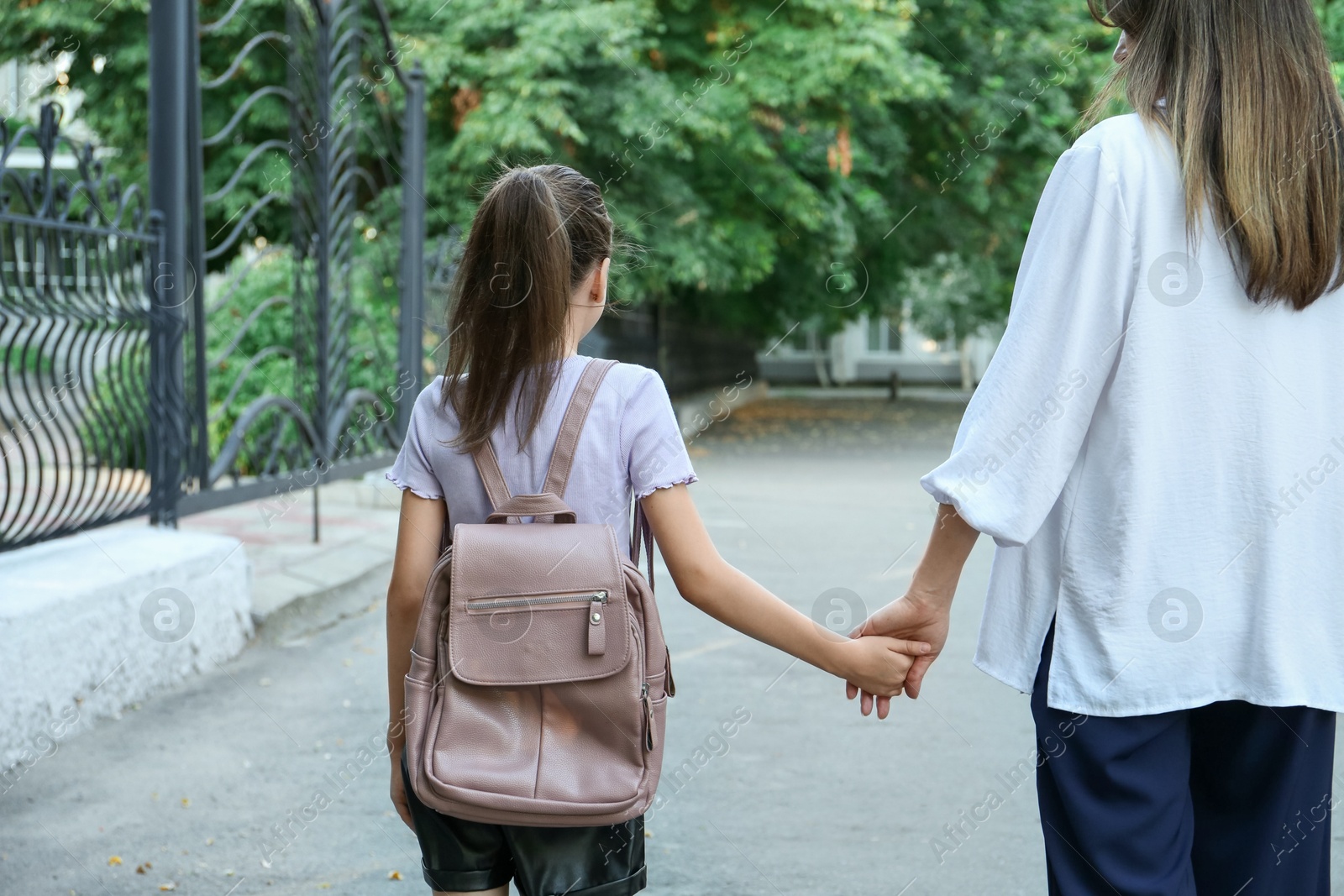 Photo of Mother and daughter holding hands outdoors, back view