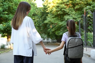 Photo of Mother and daughter holding hands outdoors, back view