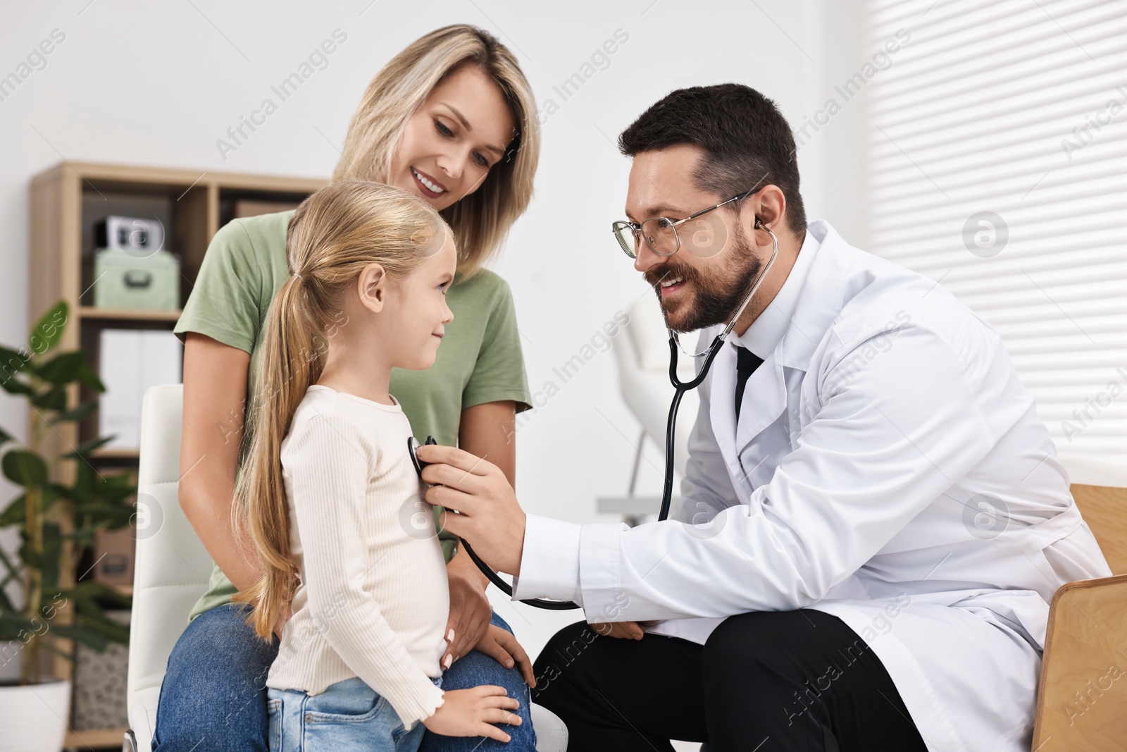 Photo of Doctor examining little girl with stethoscope and her mother in hospital