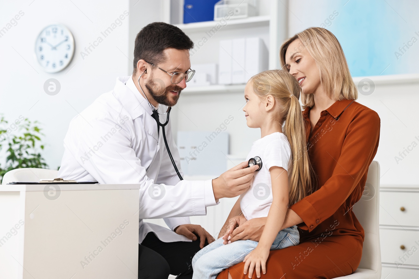 Photo of Doctor examining little girl with stethoscope and her mother in hospital