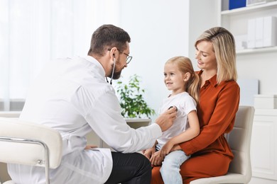 Photo of Doctor examining little girl with stethoscope and her mother in hospital