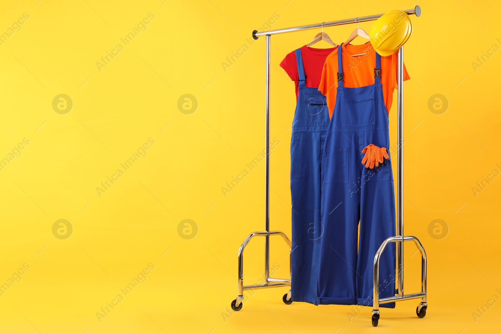 Photo of Workers' uniforms on clothing rack against yellow background. Space for text